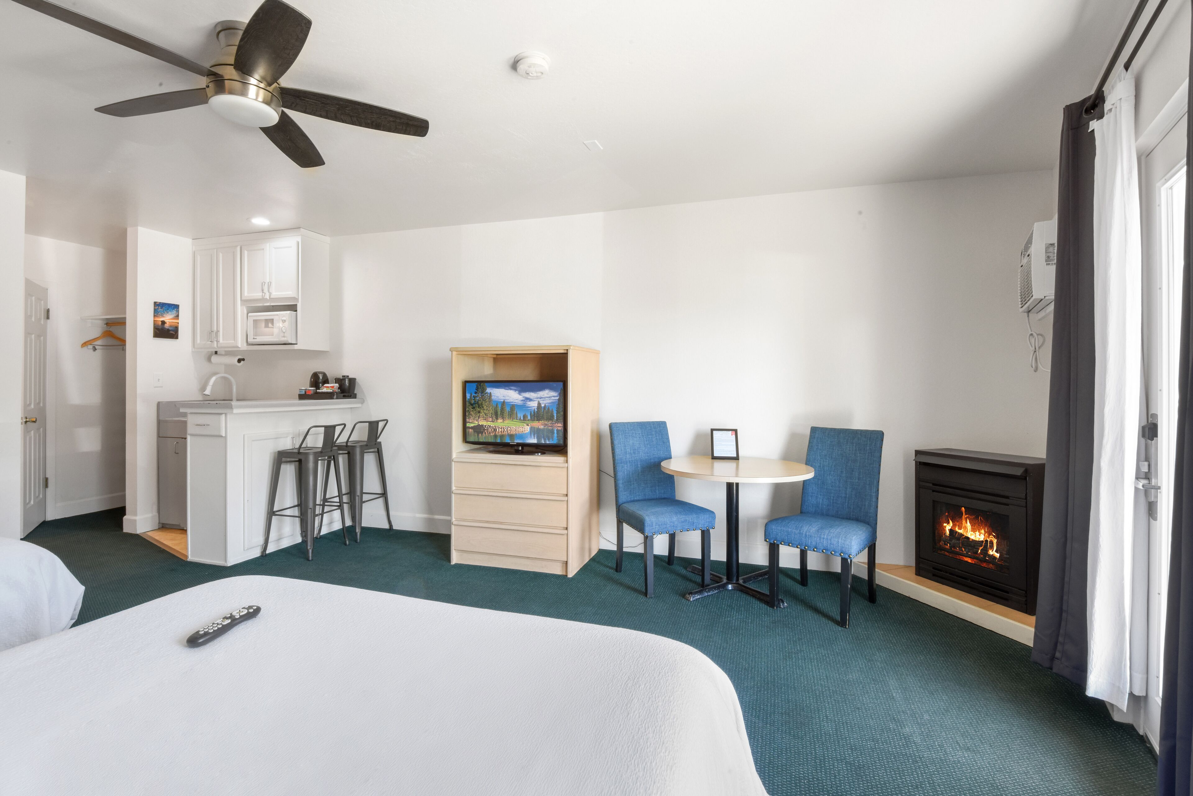 A hotel room with a bed, a desk with a TV, a fireplace, and a ceiling fan.