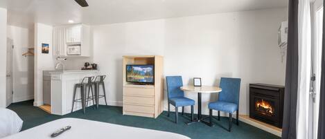 A hotel room with a bed, a desk with a TV, a fireplace, and a ceiling fan.