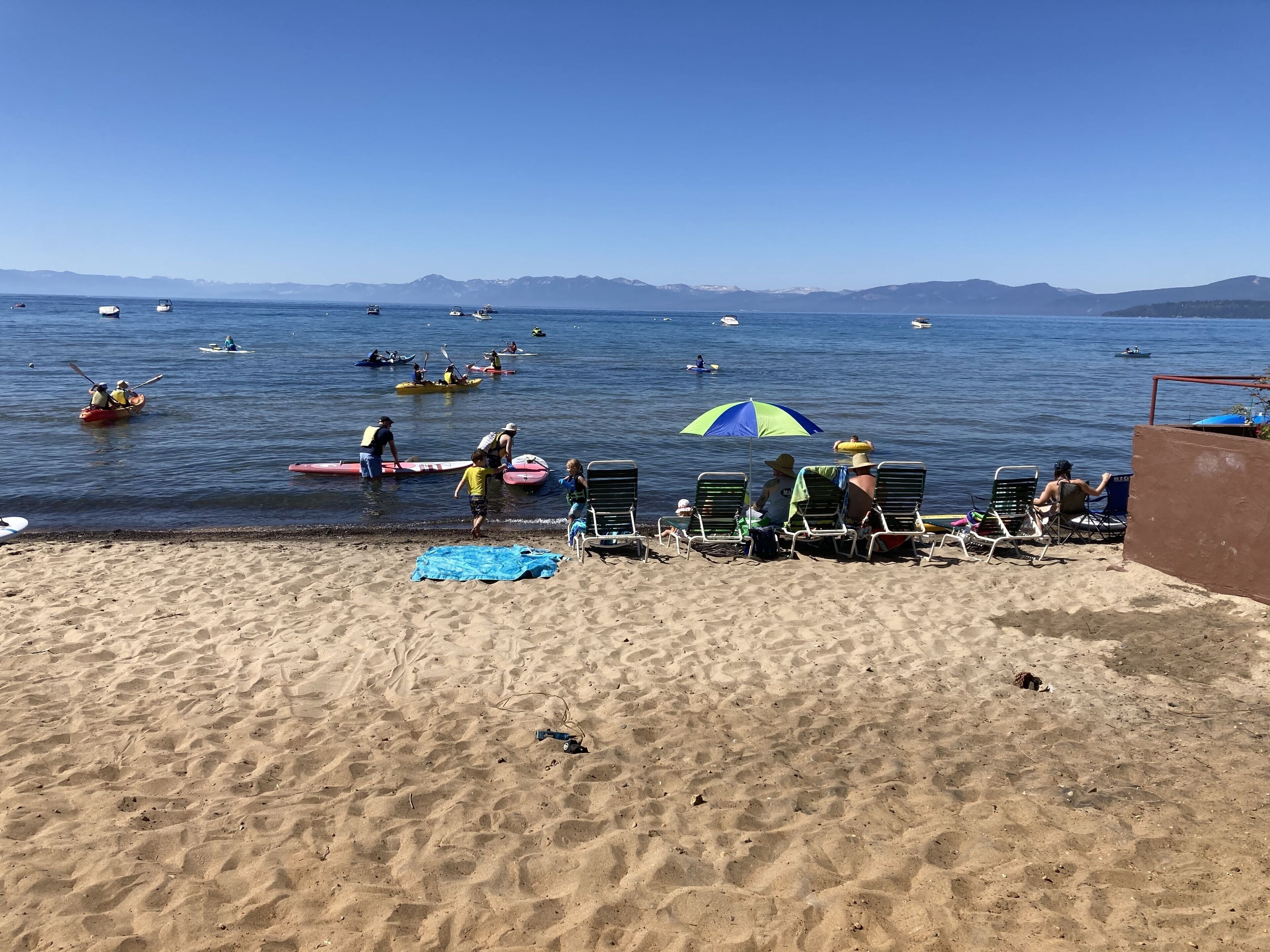 A beach with several kayaks and canoes on the water, a few people in the water, and beach chairs and umbrellas on the sand.