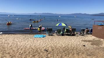 A beach with several kayaks and canoes on the water, a few people in the water, and beach chairs and umbrellas on the sand.