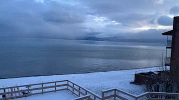 Une terrasse enneigée offrant une vue sur une étendue d’eau calme et sur des montagnes lointaines.