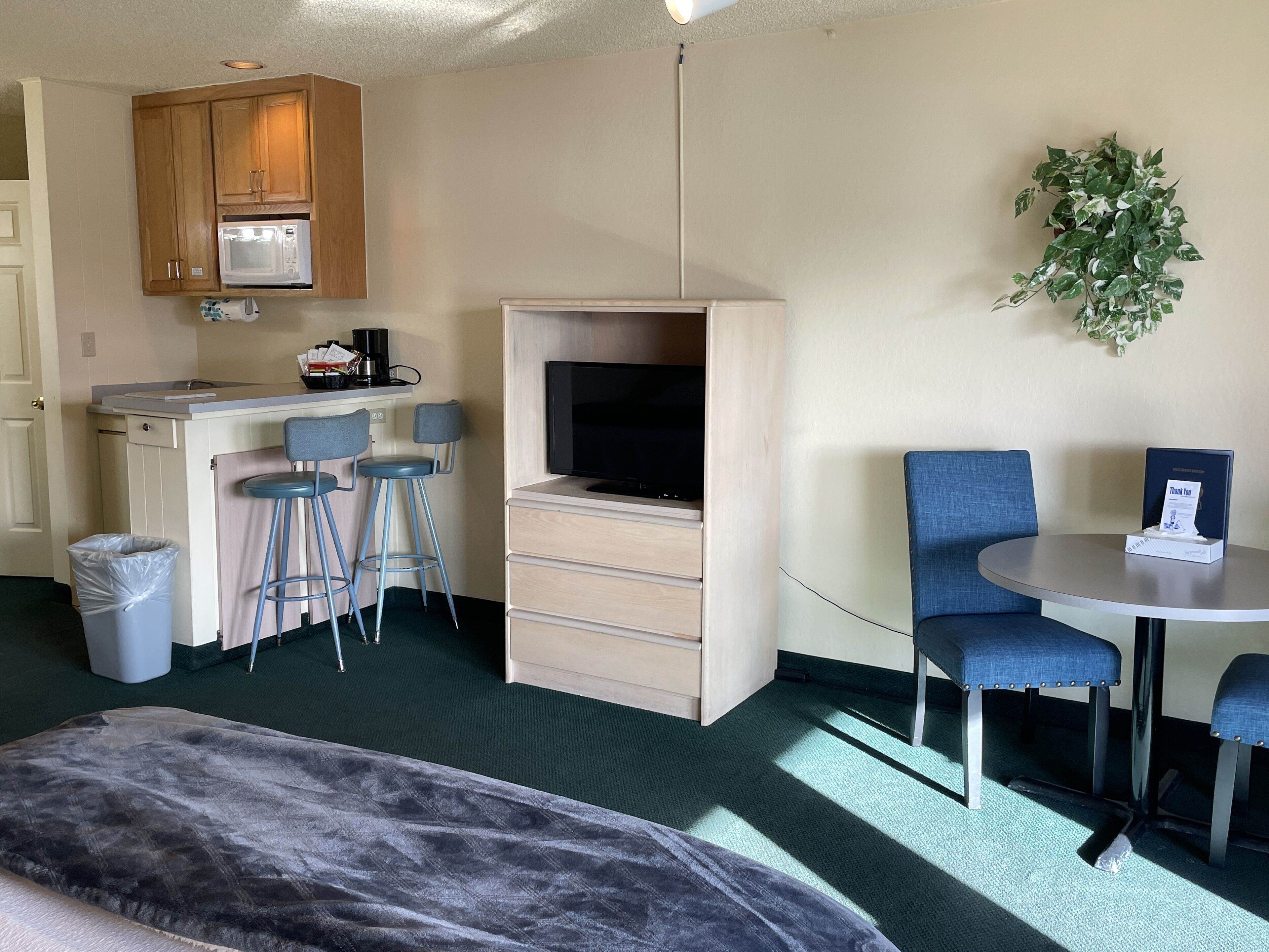 A compact hotel room with a kitchenette, a TV, a small dining area, and a large window.