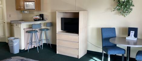 Habitación de hotel compacta con kitchenette, televisor, pequeño comedor y ventana grande.