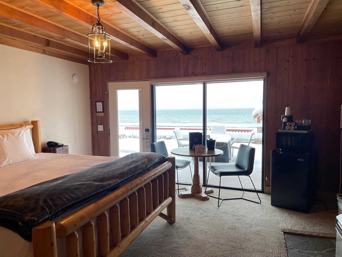 A bedroom with a bed, a desk, a chair, a coffee machine, and a view of the ocean.