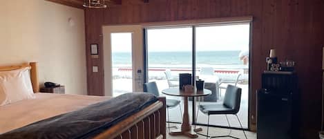 Un dormitorio con cama, escritorio, silla, cafetera y vista al océano.