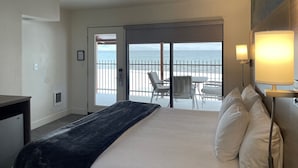 Habitación de hotel con cama, escritorio, silla, mesa y balcón con vista al mar.