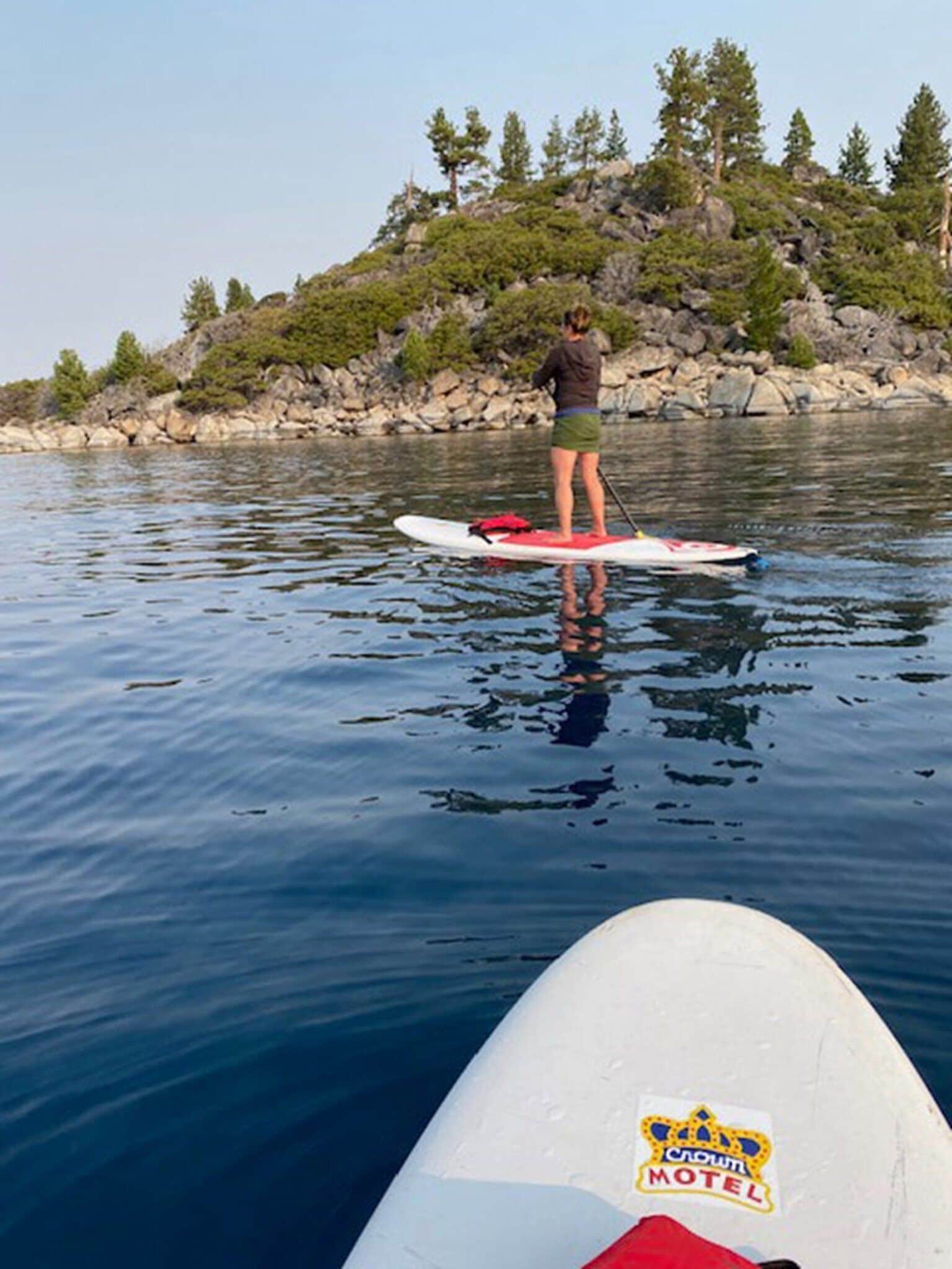A person standing on a paddleboard in a body of water with a rocky shoreline and trees in the background.