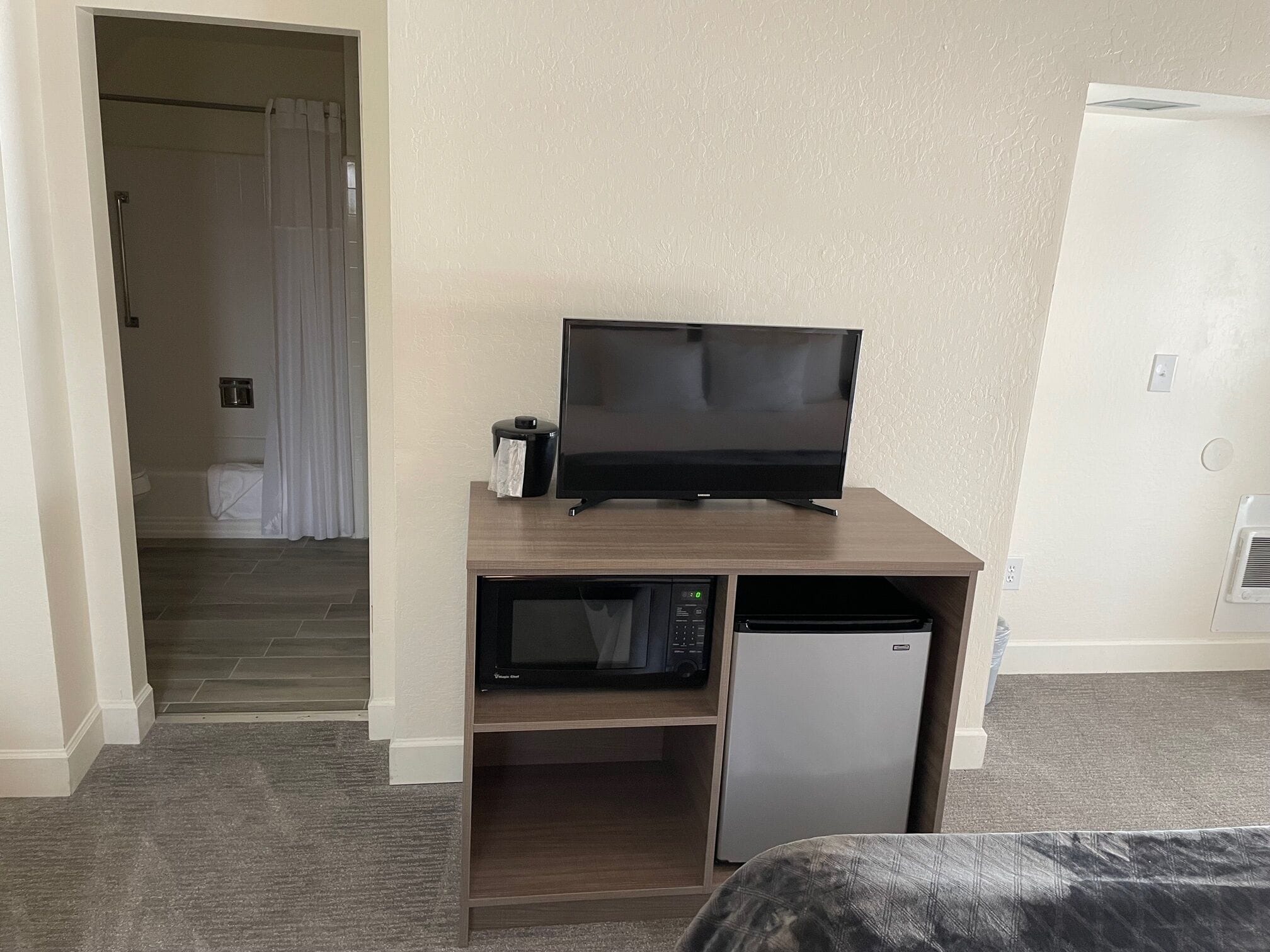 Una camera d'albergo con televisore su supporto in legno, forno a microonde e mini-frigorifero.