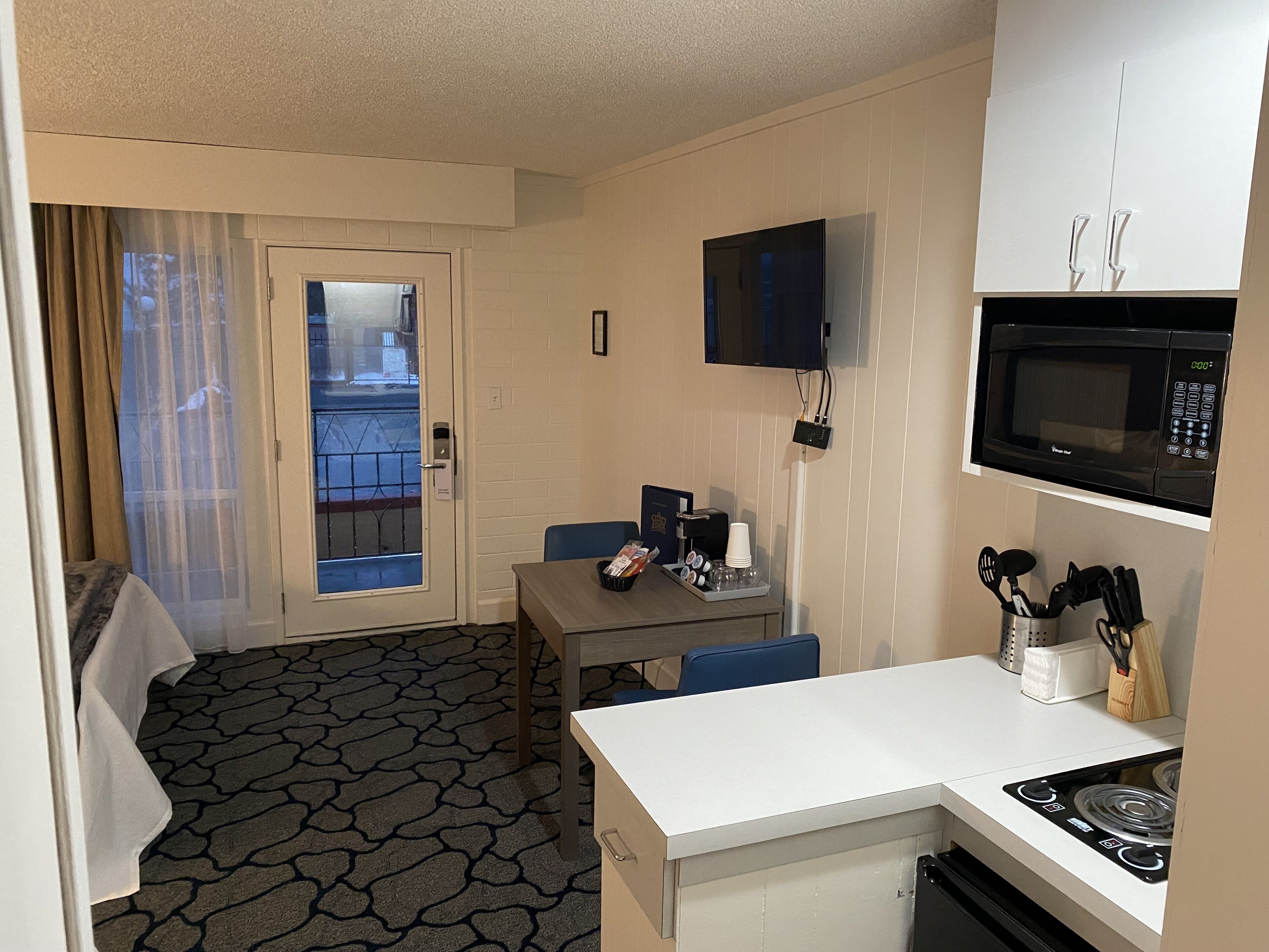 Une chambre d’hôtel compacte dotée d’une kitchenette, d’un coin repas et d’une porte donnant sur un balcon.