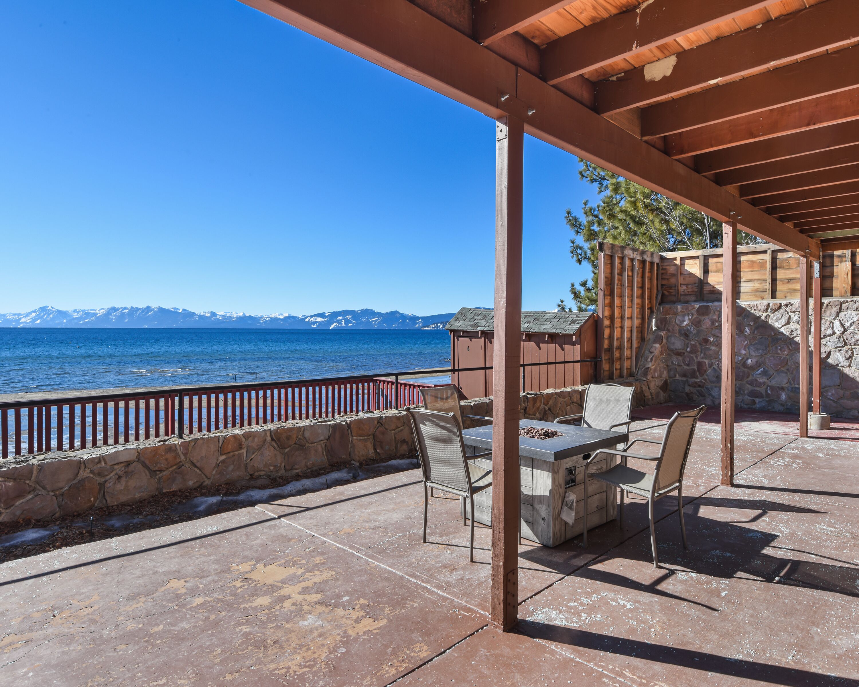 A covered outdoor seating area with a stone wall and a view of the sea and mountains.