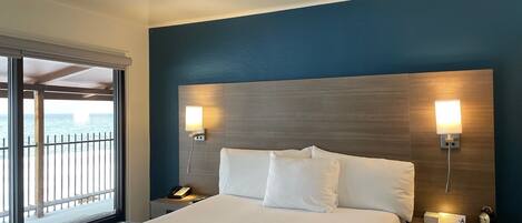 A hotel room with a large bed, two bedside lamps, a nightstand, and a view of the sea through a window.