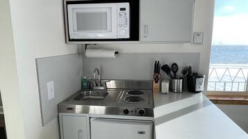 A compact kitchen with a microwave, stove, and refrigerator, featuring a view of the sea through a window.