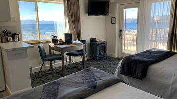 Quarto de hotel com duas camas, uma escrivaninha com cadeira, uma mesinha com um livro, televisão e vista para o mar.