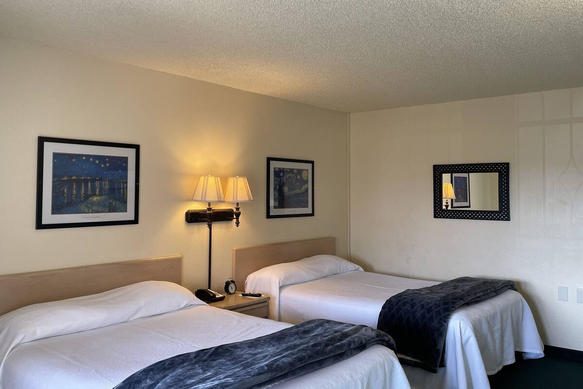 A hotel room with two beds, a nightstand with a lamp, and two framed artworks on the walls.