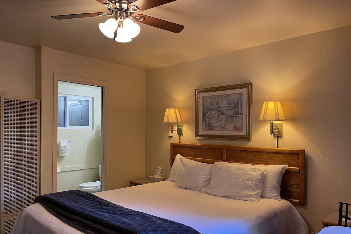 A hotel room with two beds, a ceiling fan, wall-mounted lamps, a framed picture, and a window.