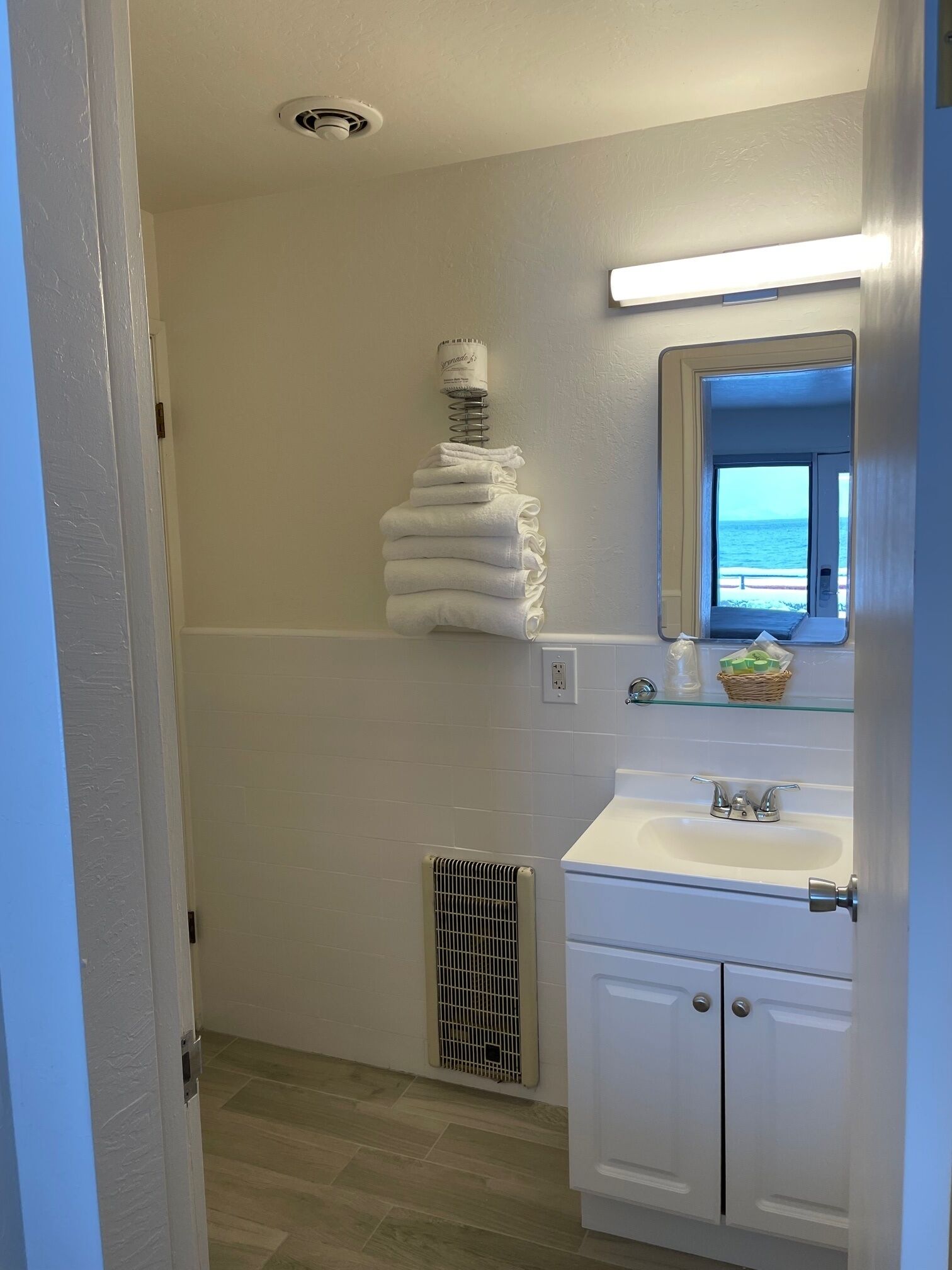 Une salle de bain avec un lavabo blanc, un miroir et un porte-serviettes sur lequel sont pliées des serviettes.