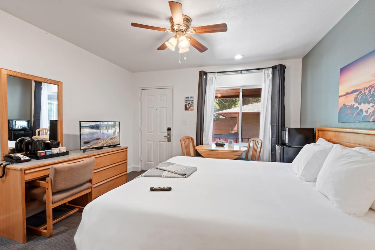 A hotel room with a bed, desk, chair, ceiling fan, and a window with curtains.