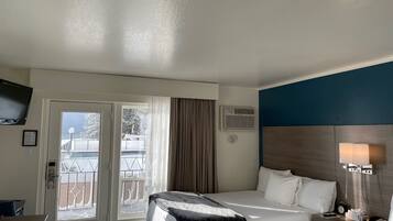 Habitació d'hotel amb llit, taulell de nit, làmpada i vista a un balcó cobert de neu.