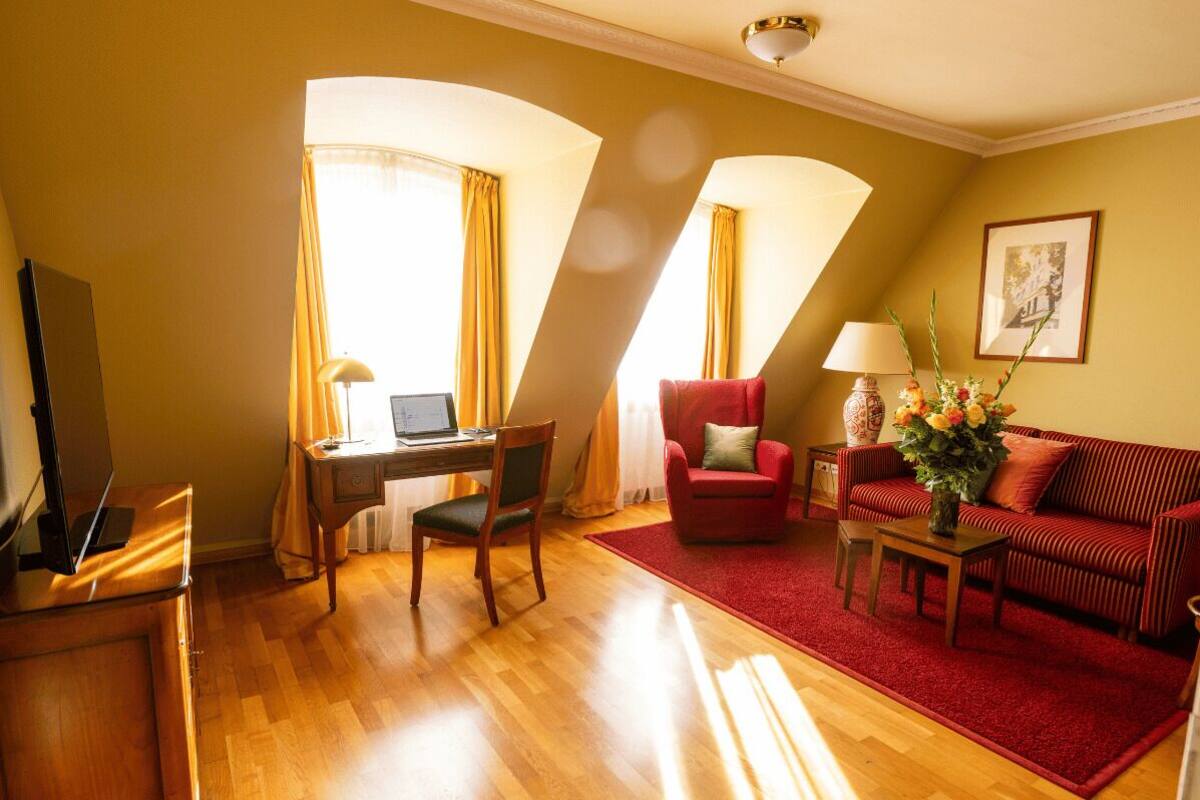 A room with a wooden desk, a red armchair, a striped sofa, and a red carpet.