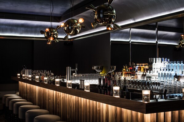 A bar area with a wooden counter, multiple stools, and hanging spherical light fixtures. - Louisa's Place (Berlin)