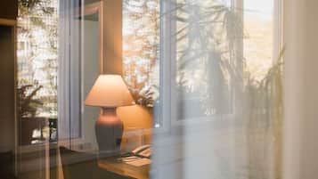 A room with a desk, a lamp, and a telephone. There is a window with a view of trees and a building outside.