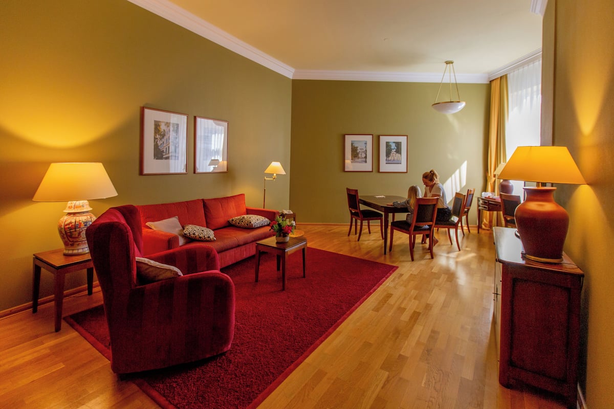 A living room with a red sofa, a dining table, and chairs. There are two lamps on side tables.