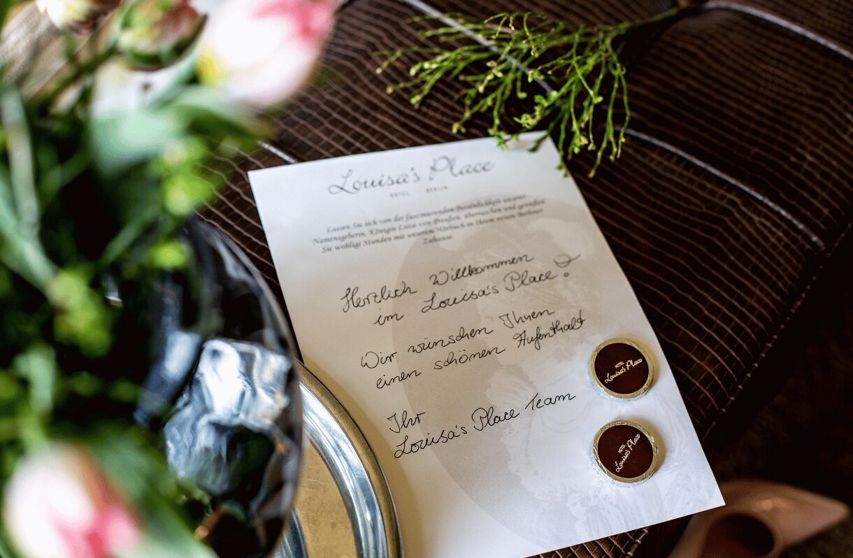 A menu card titled "Louisa's Place" with a handwritten note and two small round seals.