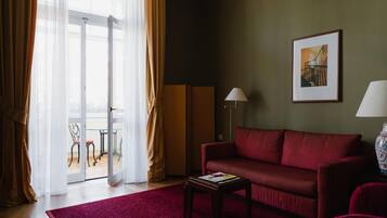 A room with a red sofa, a small table with a magazine, a lamp, a framed picture on the wall, and a view through a glass door.