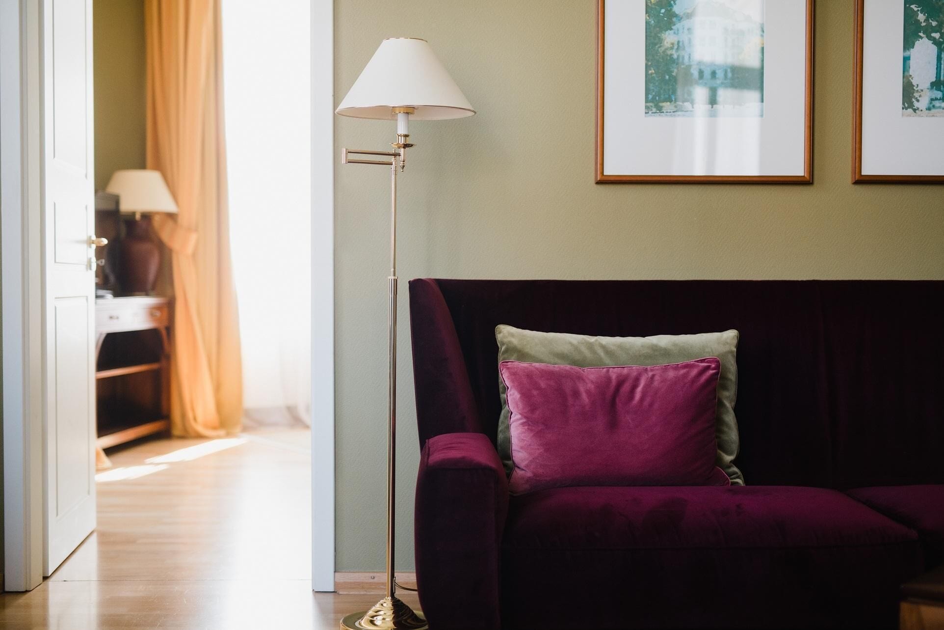 Una habitación con un sofá morado oscuro, una lámpara de pie y un cuadro en la pared.