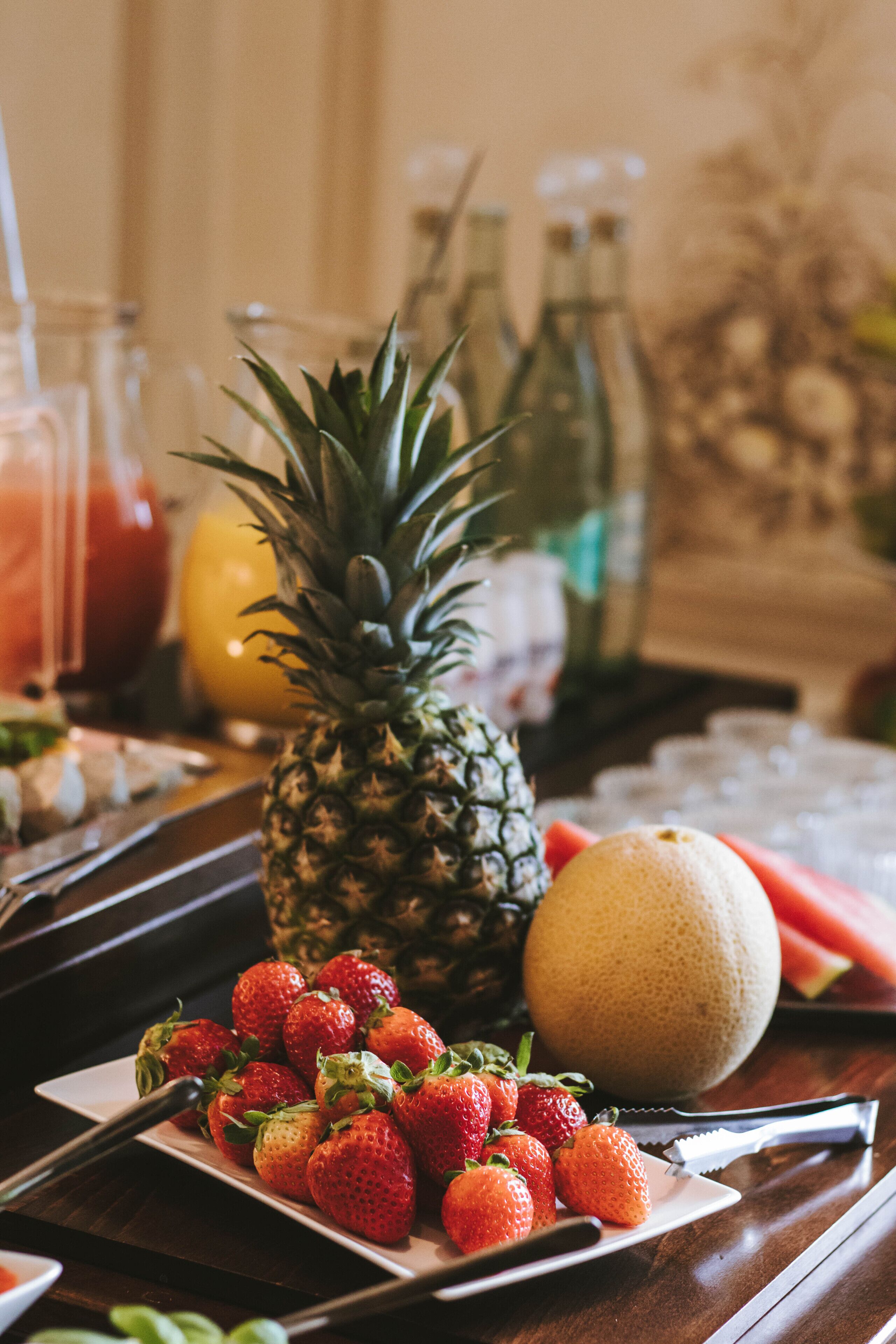 Un plat de fruita amb maduixes, una pinya i un meló cantalup sobre una taula de fusta.
