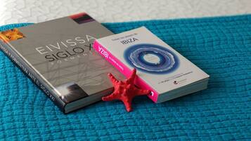 Un llit amb un almofí blau i un llibre anomenat 'Elvis A Siglo XXI' sobre un edredó blau amb textura.