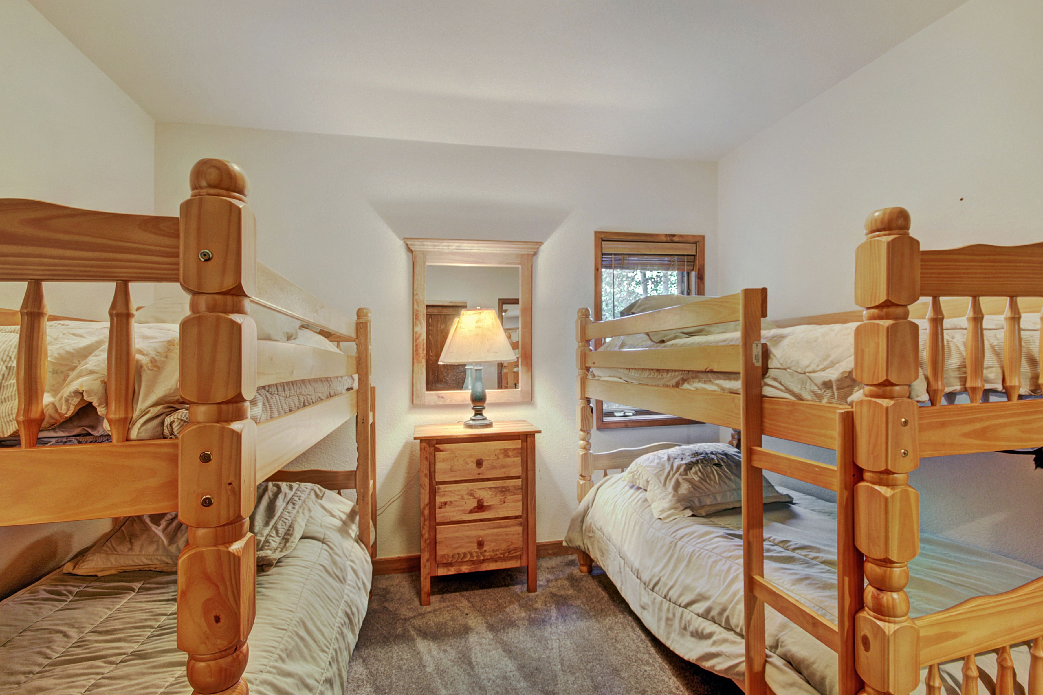 A room with three wooden bunk beds, a small wooden nightstand with a lamp, and a mirror on the wall.