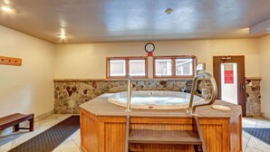 Un jacuzzi de madera con escalones, una pared de piedra, un reloj y un banco.