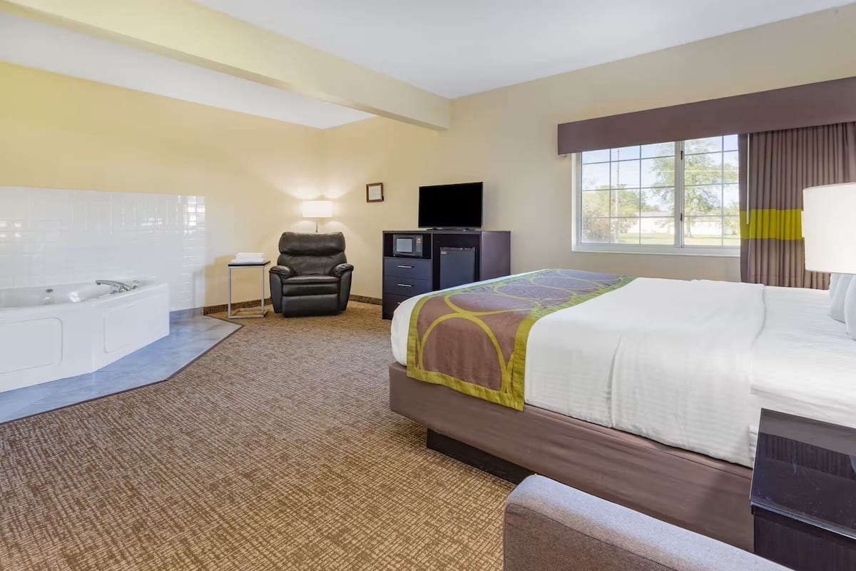 Habitación de hotel con cama, sillón de masajes, escritorio con ordenador, televisor y ventana grande.