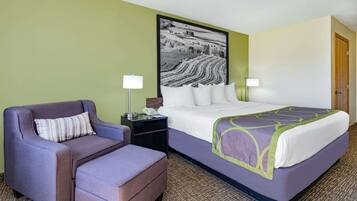 A hotel room with a bed, a chair, a nightstand, and a lamp.