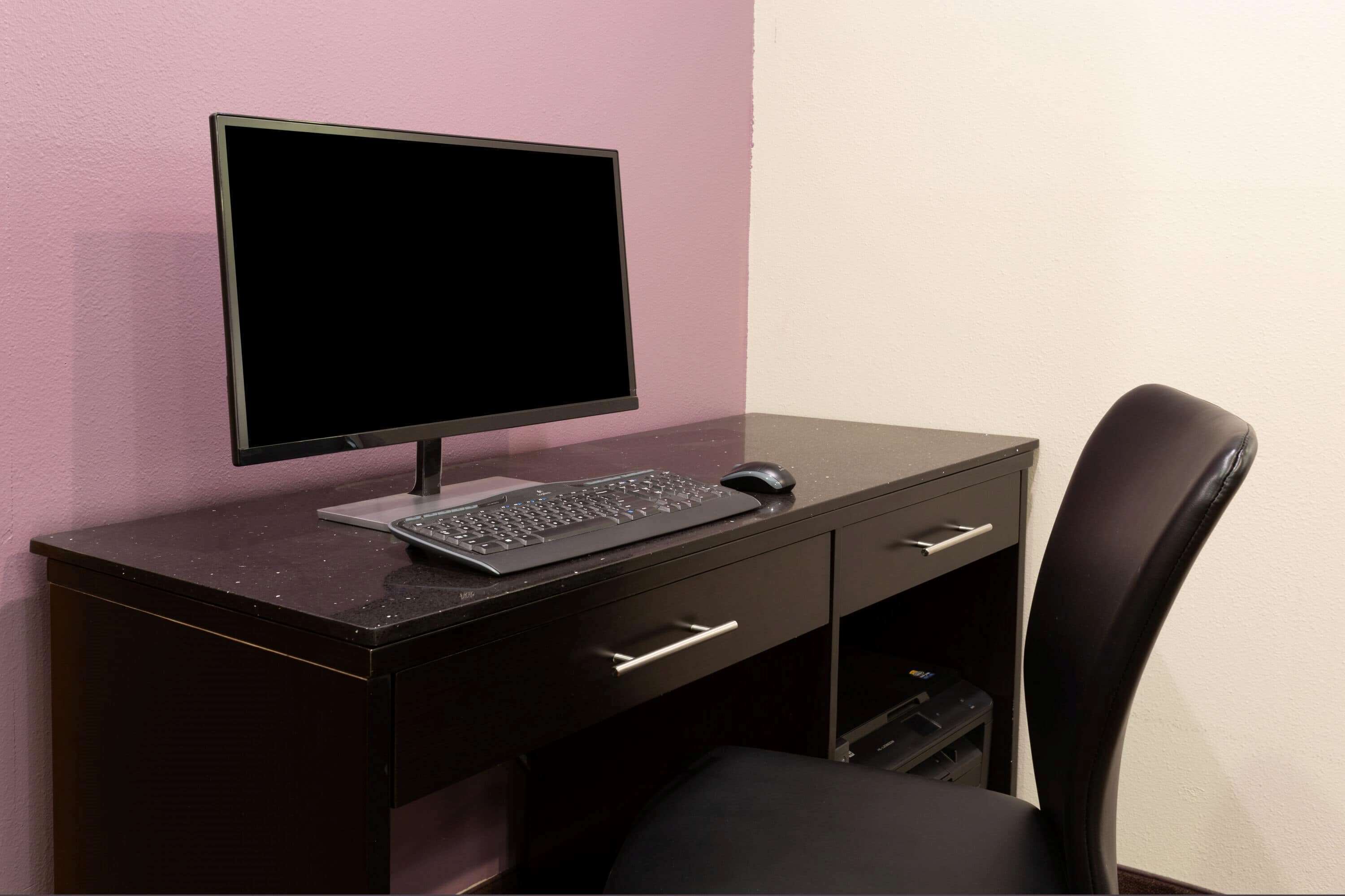 A dark wooden desk with a computer monitor, keyboard, and mouse.