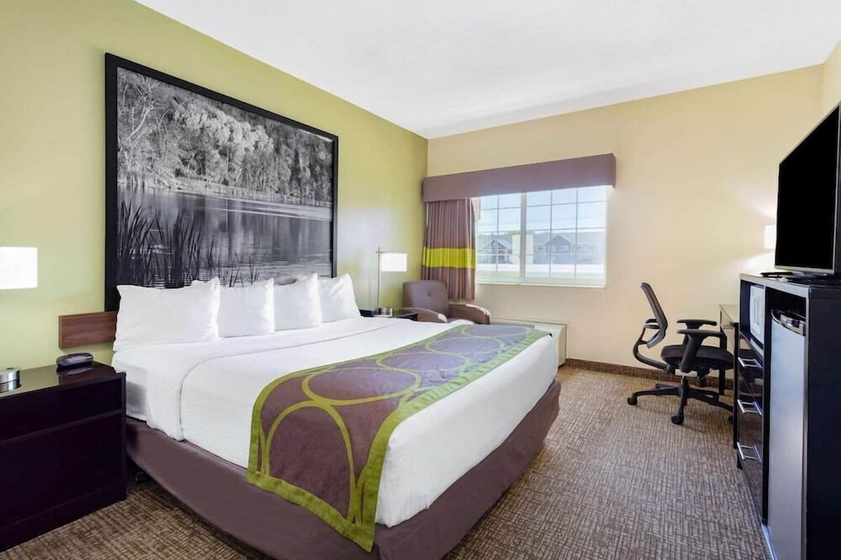 Habitación de hotel con una cama grande, un escritorio con computadora, una silla, televisor y ventana con cortinas.