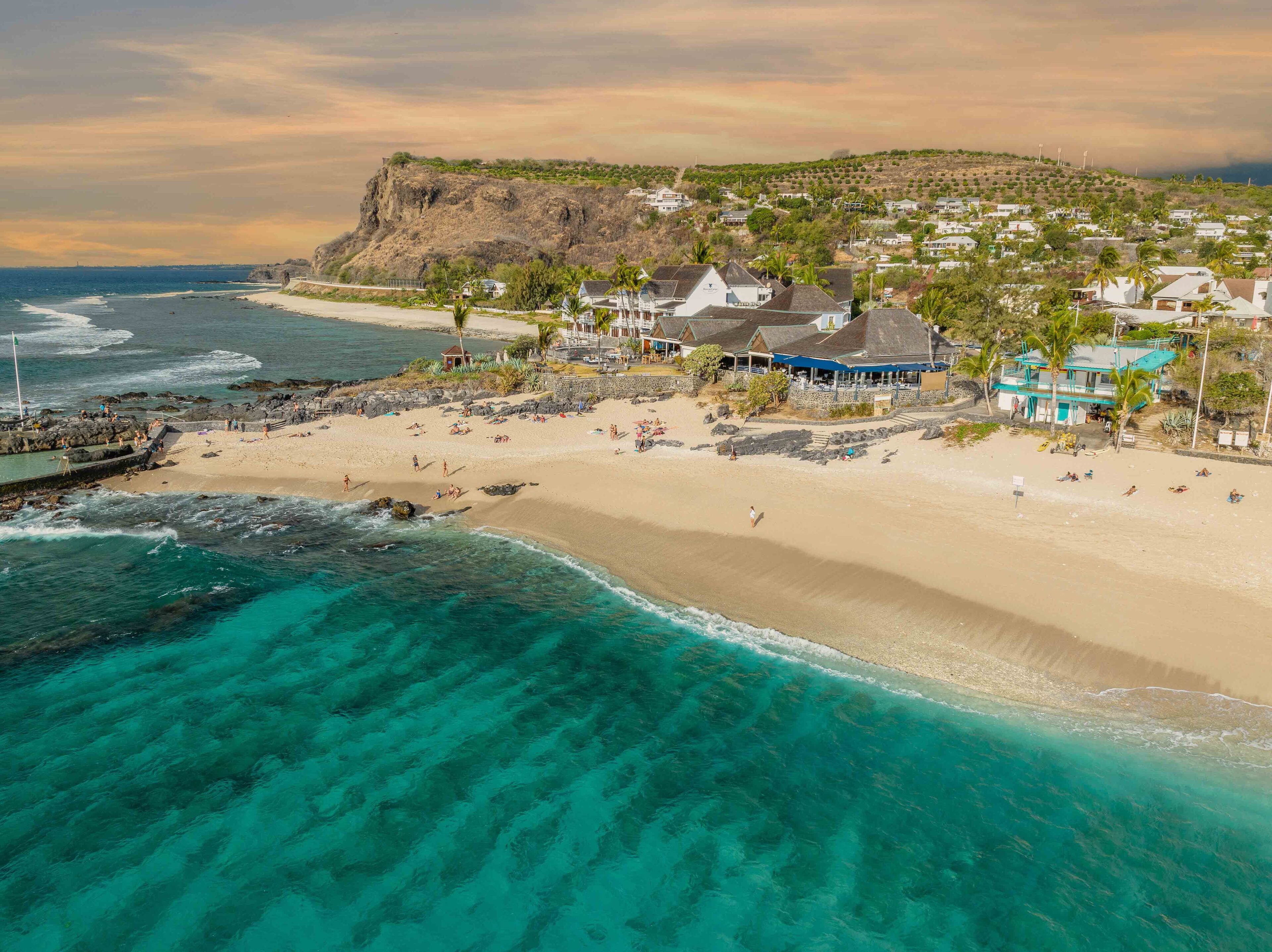 Un pueblo costero con una playa arenosa, aguas turquesas cristalinas y un acantilado rocoso.