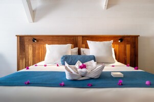 Una cama bien hecha con una colcha azul, almohadas blancas y un arreglo floral decorativo.