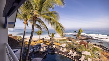 Unwind in a serene beachfront setting with a pool, lounge chairs, and umbrellas, offering a tranquil ocean view.