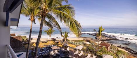 A poolside area with lounge chairs and umbrellas, overlooking a beach and ocean.