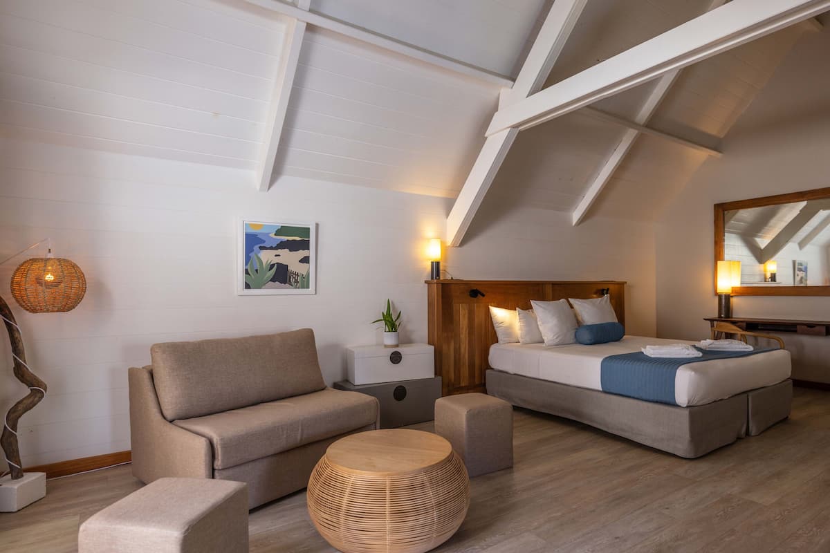 Una habitación moderna y luminosa con una cama, dos sofás, una mesita redonda y una mesita auxiliar.