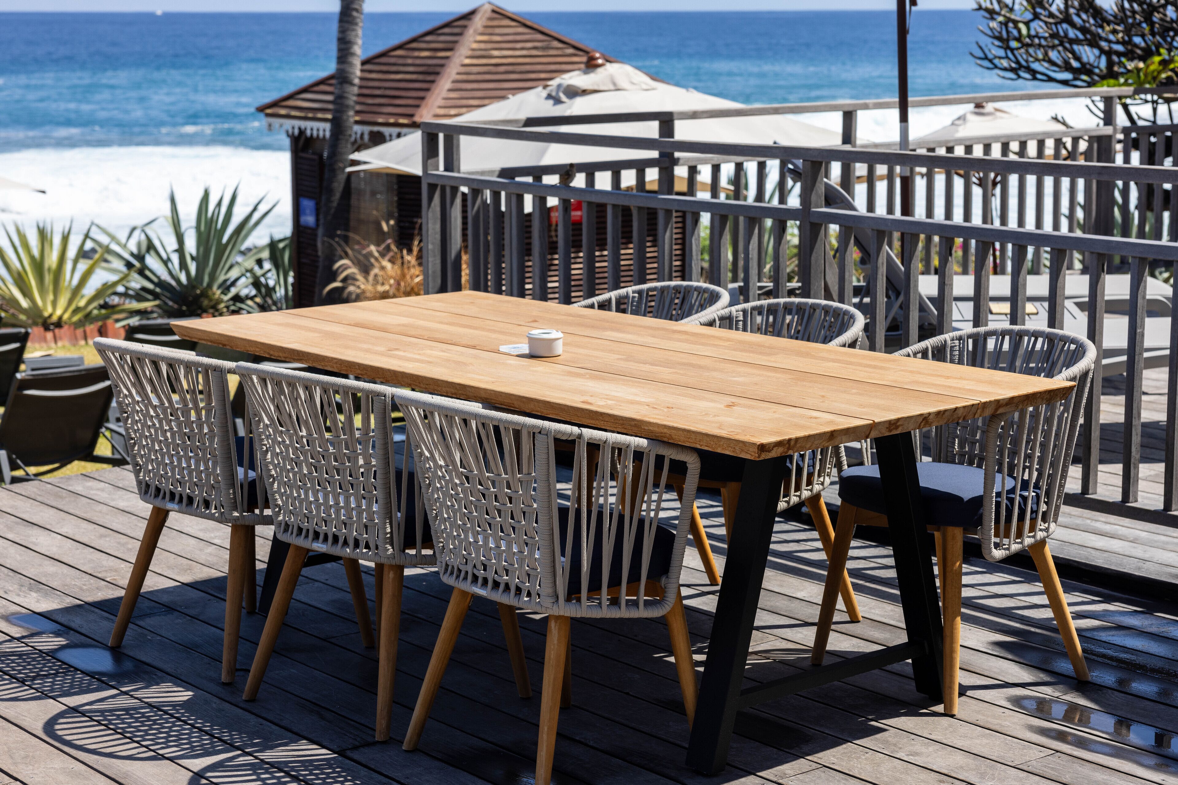 A wooden deck with a table and wicker chairs, overlooking the ocean.