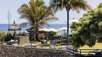 Un complexe hôtelier situé en bord de mer, doté d’une terrasse, de palmiers et offrant une vue sur l’océan.
