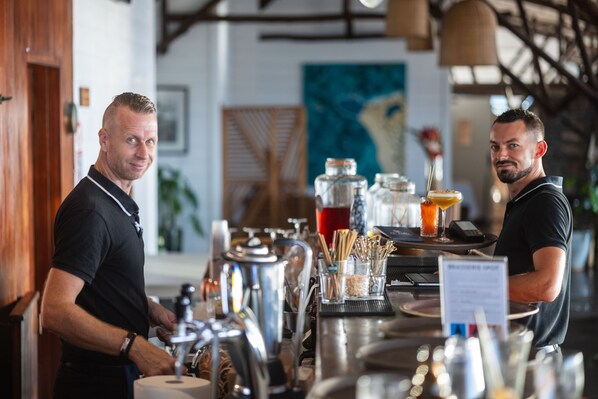 Un espace bar équipé d’appareils en acier inoxydable, d’un tableau affichant le menu, ainsi qu’une variété de verres et de bouteilles.