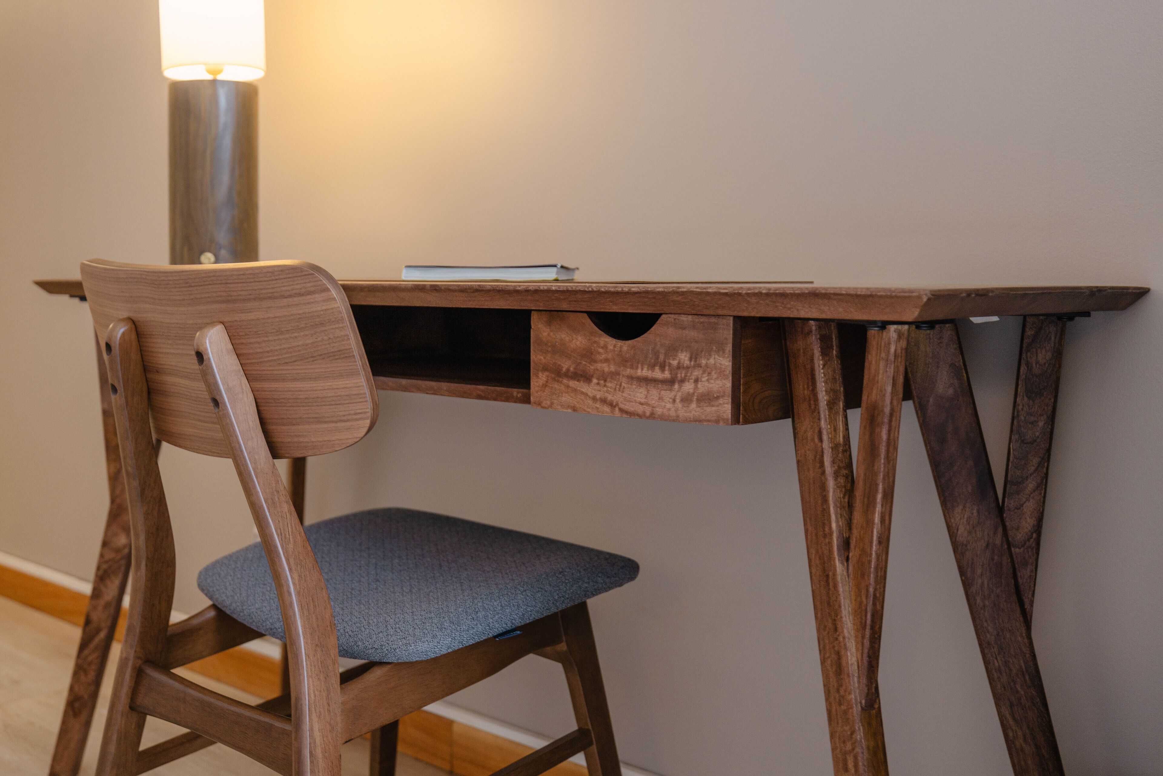A wooden desk with a chair, a lamp, and a book.