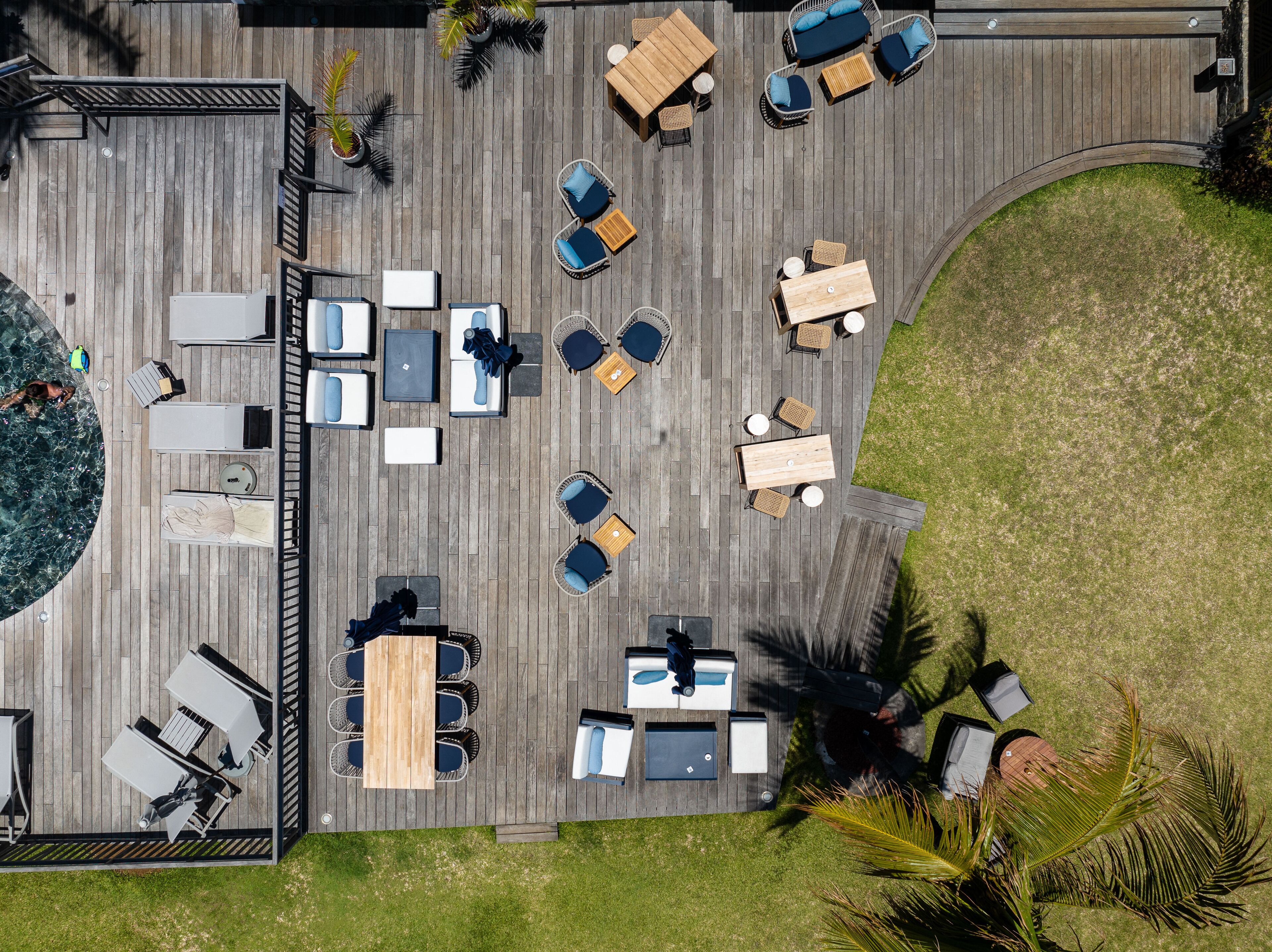 Vue aérienne d’une terrasse avec des espaces de détente en plein air, comprenant des tables et des chaises, entourée d’une plateforme en bois et d’une zone herbeuse.