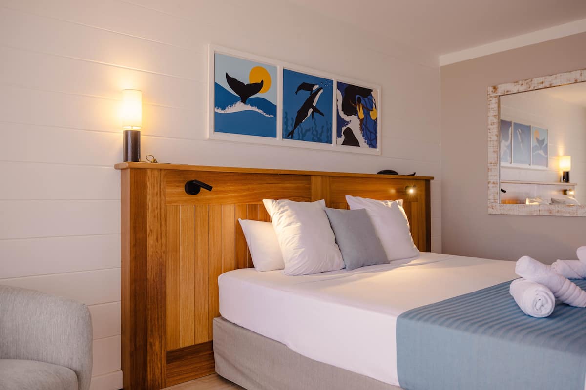 Habitación de hotel con cabecera de madera, cama con ropa de cama blanca y una obra de arte con ballenas en la pared.