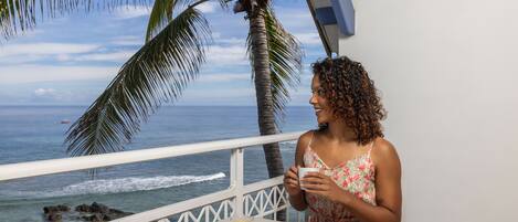 A person sitting at a table with a book and a glass of orange juice, overlooking the ocean with palm trees in the background.