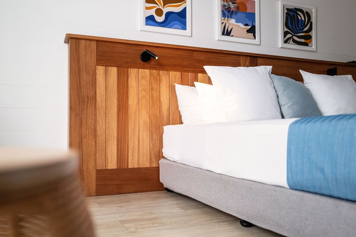Un dormitorio con cabecera de madera, ropa de cama blanca y una obra de arte en la pared.